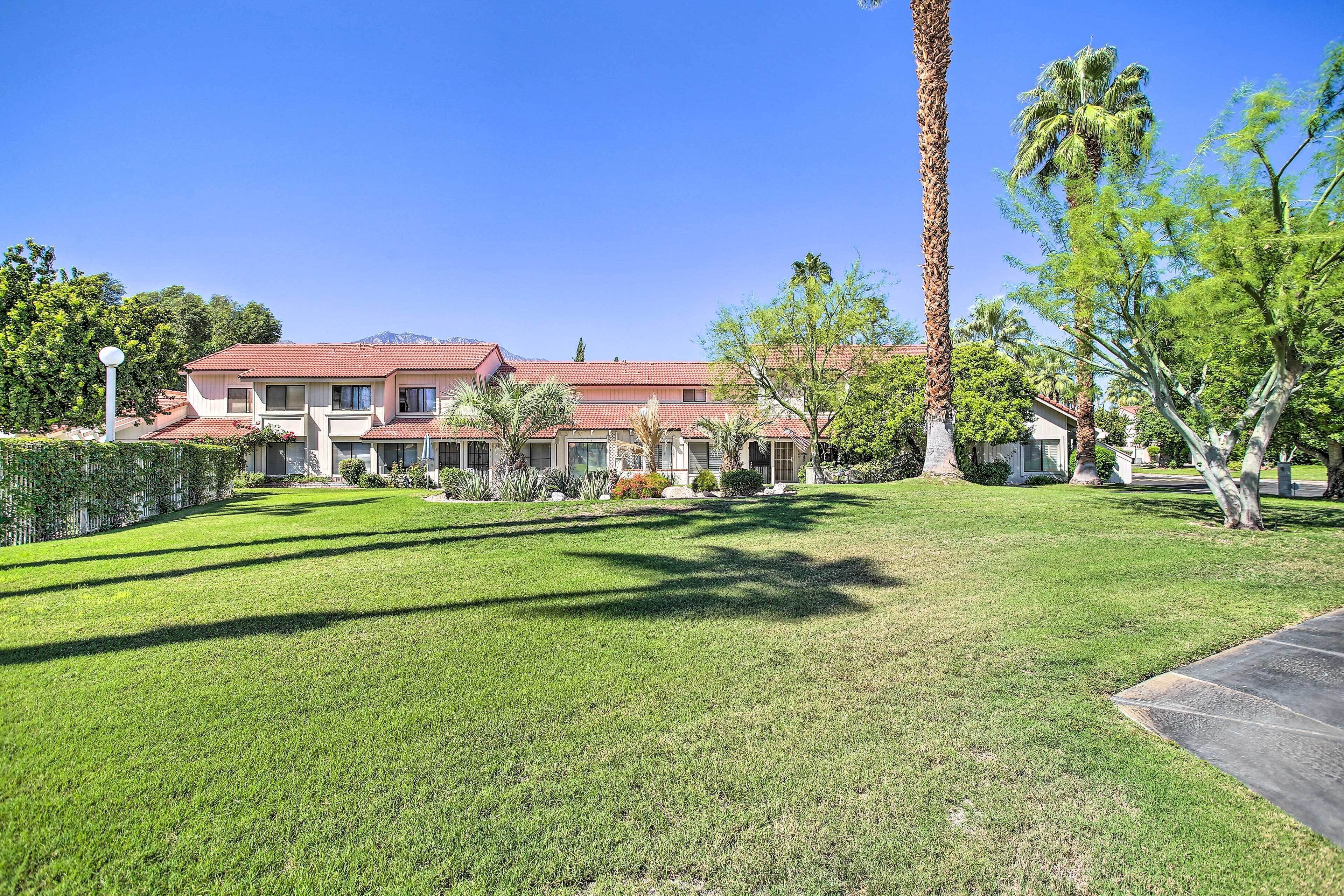 A residential area with a well-maintained lawn, palm trees, and a building with a red-tiled roof.