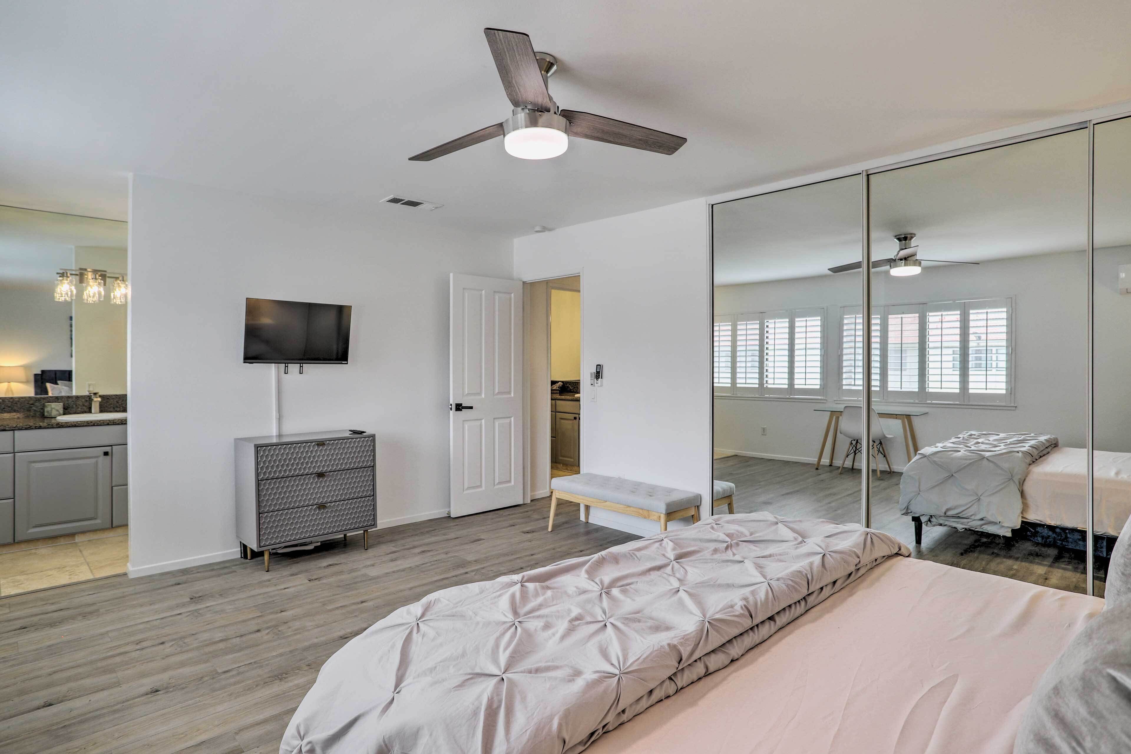 A modern bedroom with a bed, a ceiling fan, a TV, and a large mirror.