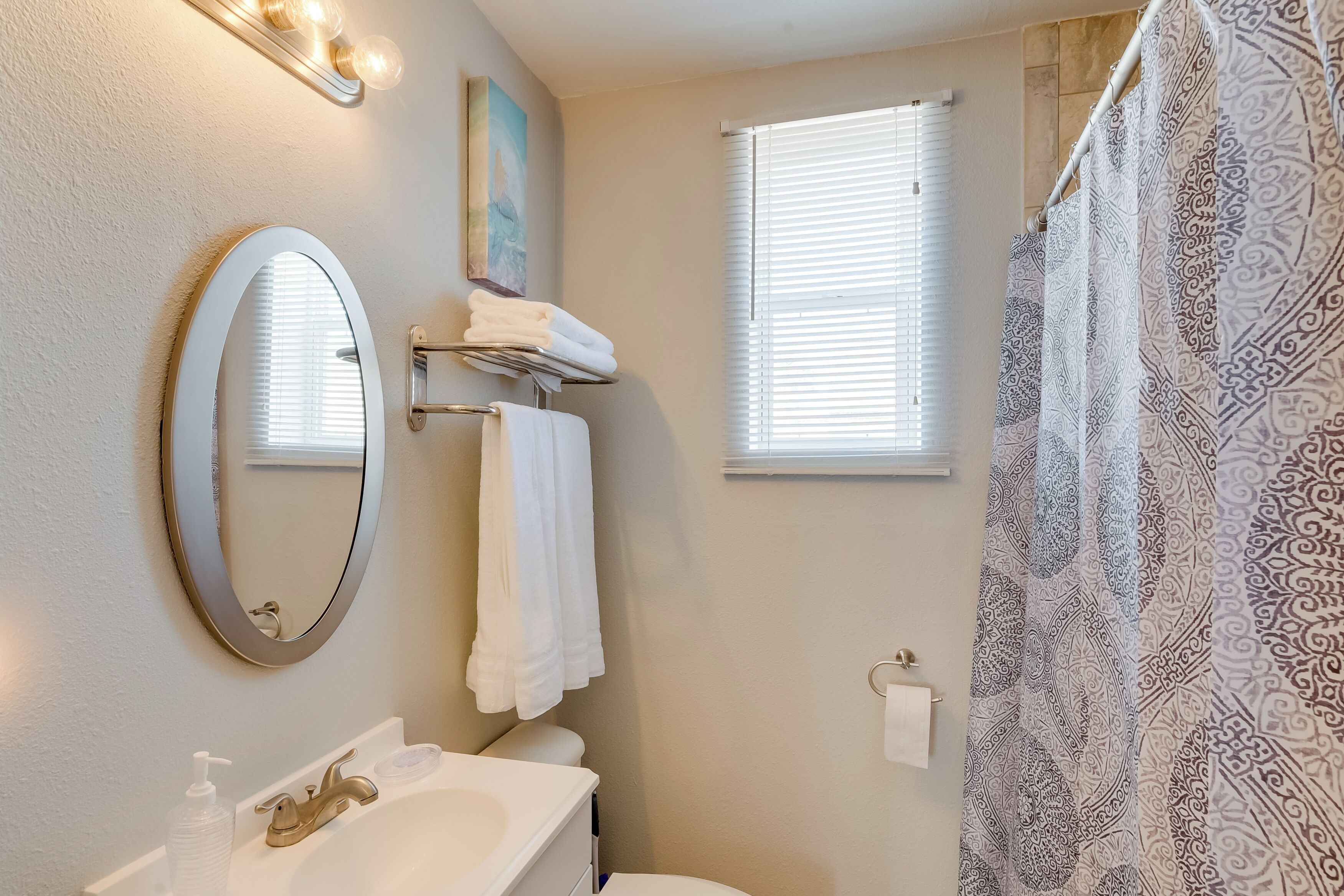 Un bagno con lavandino, specchio, porta asciugamani e tenda da doccia fantasia.