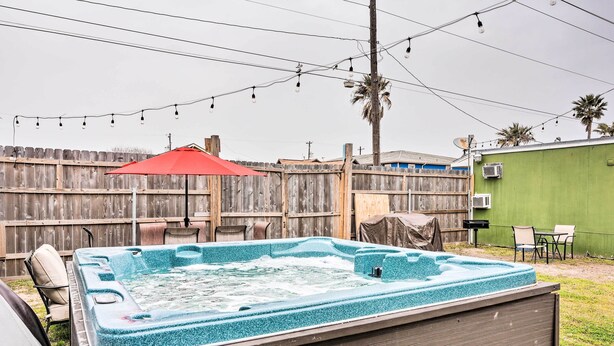 Un jacuzzi con muelle de madera, una sombrilla roja y una valla de madera al fondo.