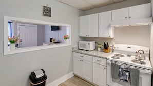 Una cocina con armarios blancos, microondas, hervidor y un cesto de basura.