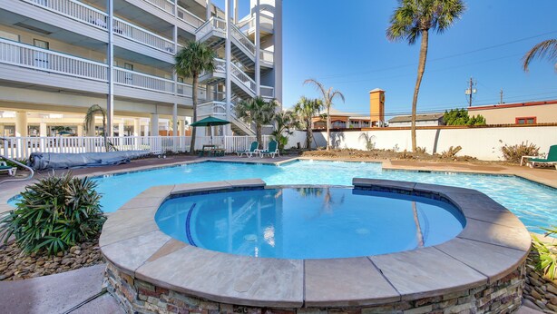 A hotel with a pool area, including a hot tub, lounge chairs, and palm trees.
