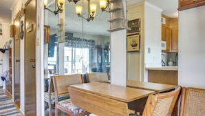 A dining area with a wooden table and chairs, a chandelier, and a view into the kitchen.
