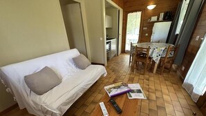 A cozy room with a white sofa, a wooden table, and a dining area with a table and chairs. - Les Ajoncs - Brocas - Gîte (BROCAS)