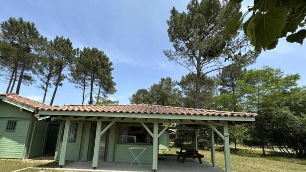 A green building with a tiled roof, a covered patio area, and a picnic table. - Les Ajoncs - Brocas - Gîte (BROCAS)