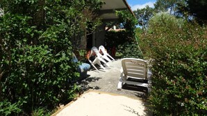 A covered outdoor seating area with a bench and a table, surrounded by greenery. - Le Gîte du Pont Blanc (ST-JULIEN-EN-BORN)