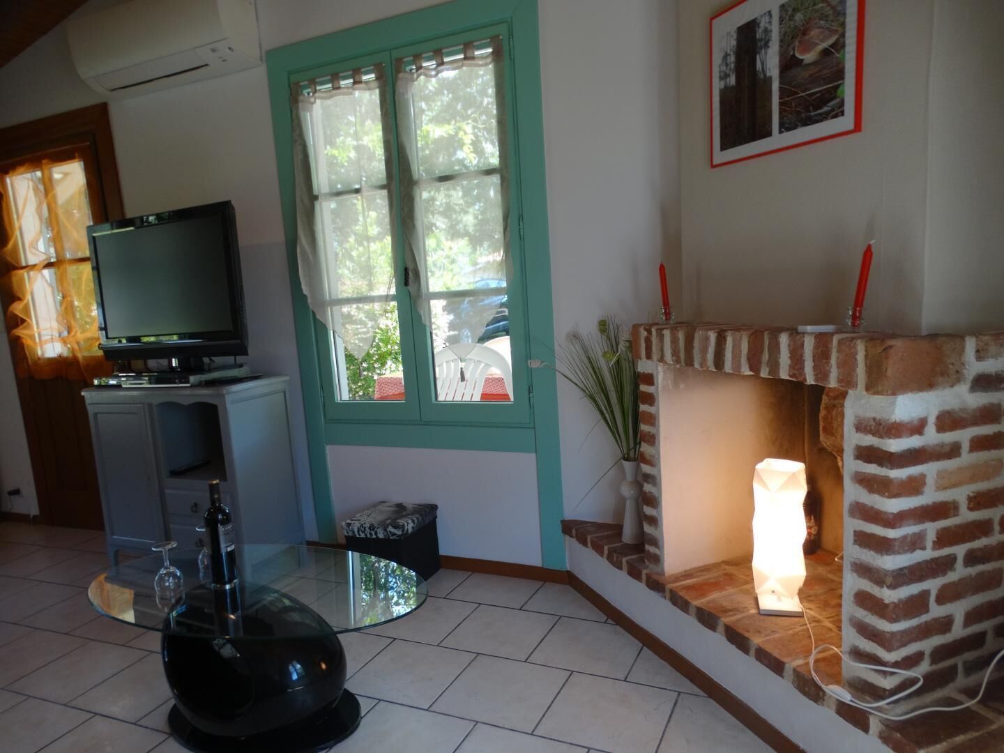 Ein Wohnzimmer mit Fernseher, Glastisch, Kamin und einem Fenster mit Vorhängen.