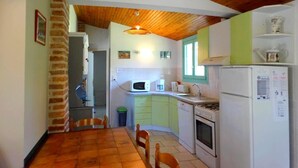 A compact kitchen with a wooden ceiling, a dining table, and basic appliances. - Le Gîte du Pont Blanc (ST-JULIEN-EN-BORN)