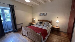 A bedroom with a wooden bed, two bedside tables with lamps, a window with curtains, and a door. - Lacoste 2 - ORX - Gîte (ORX)