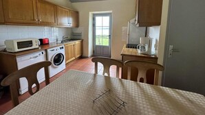 A compact kitchen with wooden cabinets, a microwave, a washing machine, and a dining table with chairs. - Lacoste 2 - ORX - Gîte (ORX)