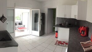 A modern kitchen with white cabinets, a red coffee machine, and a dining area with a red table and chairs. - Erable - Ste-eulalie-en-born (STE-EULALIE-EN-BORN)