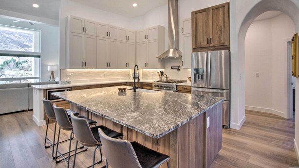 A modern kitchen with white cabinets, stainless steel appliances, a large island with bar stools, and a view of the outdoors. - Grand Junction Mountain Escape w/ Grill! (Grand Junction)