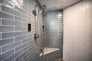 Uma casa de banho moderna com paredes revestidas a azulejos cinzentos, um banco embutido e um chuveiro com um chuveiro de mão.