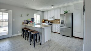 A modern kitchen with white cabinets, a large island with stools, stainless steel appliances, and a window providing natural light. - Las Vegas Retreat w/ Yard < 5 Mi to Strip! (Las Vegas)