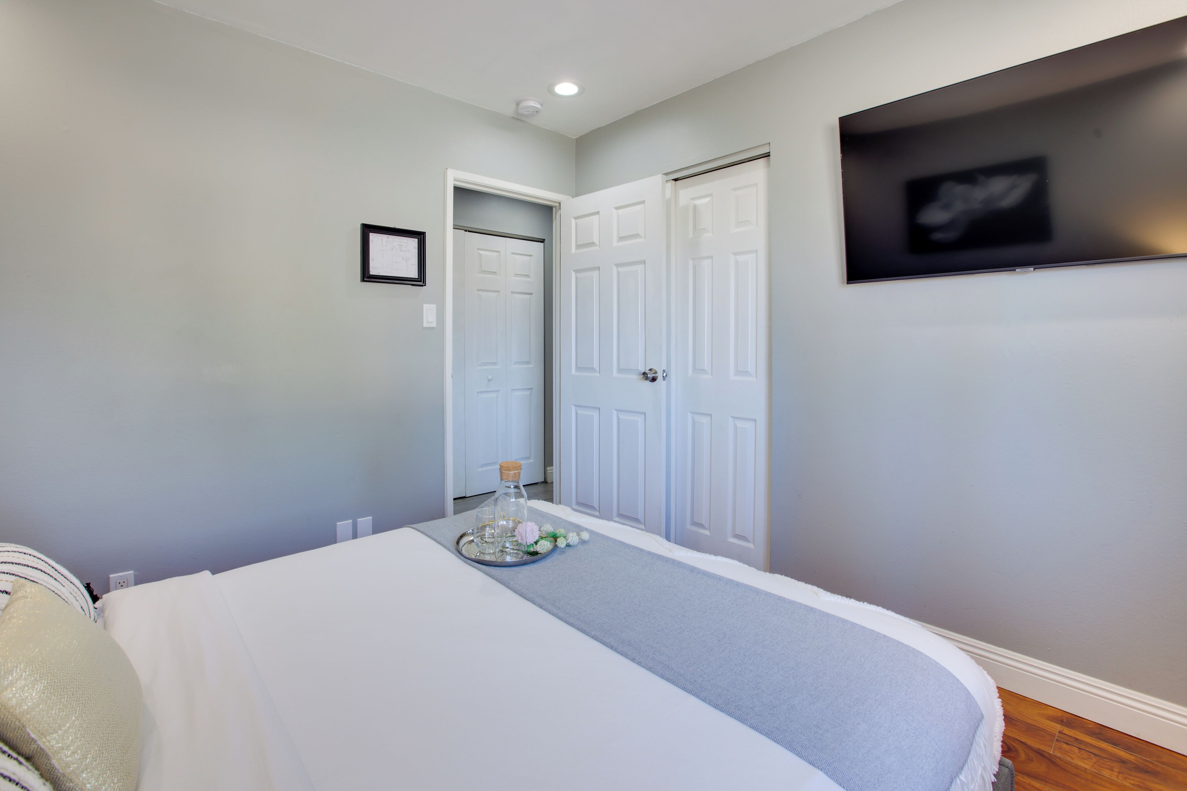A bedroom with a bed, a bedside table with a tray, a framed picture, and a door.