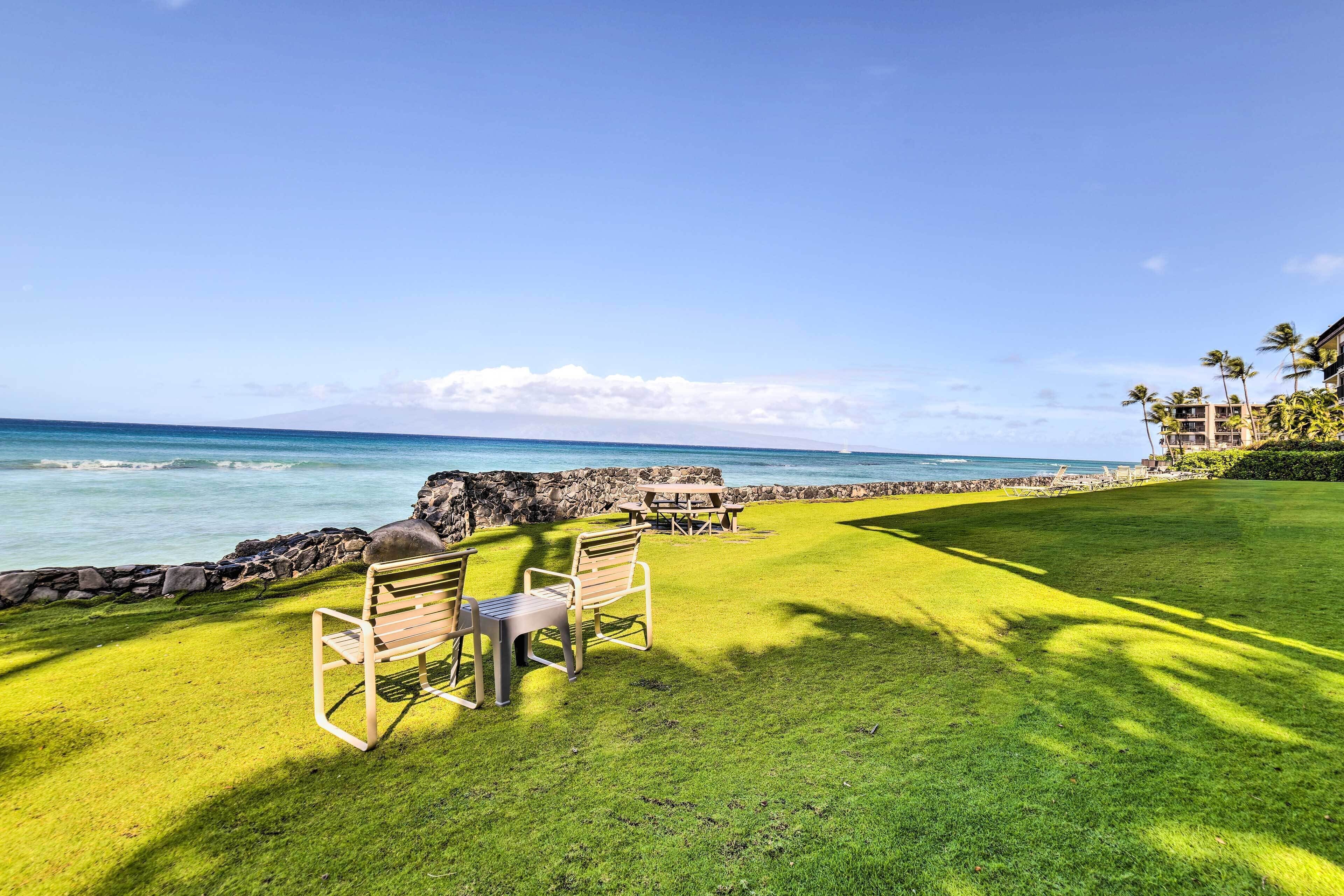 A grassy area with a bench and picnic table, a stone wall, and a view of the ocean.