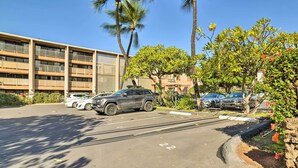Un parcheggio con diverse auto, un edificio a più piani con balconi e palme.