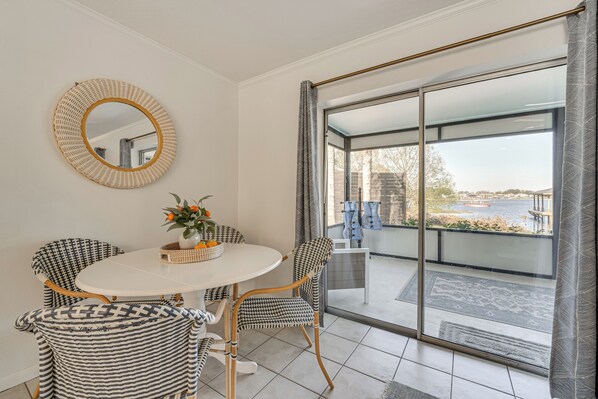 A dining area with a round table, four chairs, a woven mirror, and a view of a balcony with a railing and a body of water. - Lakefront Retreat w/ Kayaks & Fire Pit in Clermont (Clermont)