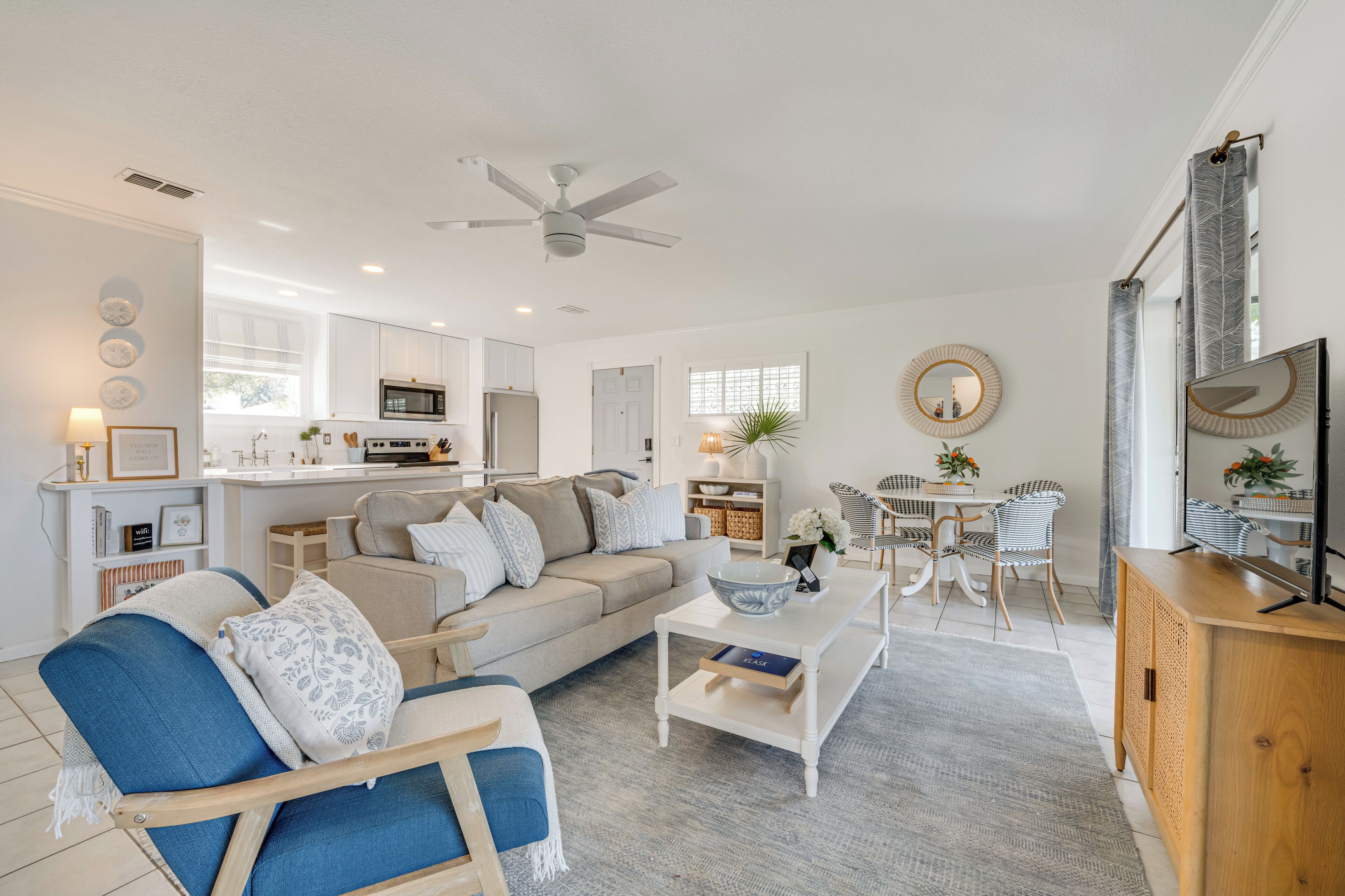 A modern living room with a sofa, coffee table, and chairs, a kitchen area with cabinets and appliances, and a dining area with a table and chairs.