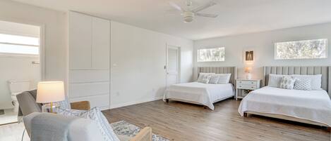 Un dormitorio amplio con dos camas, ventilador de techo y un gran ventanal que deja entrar luz natural.