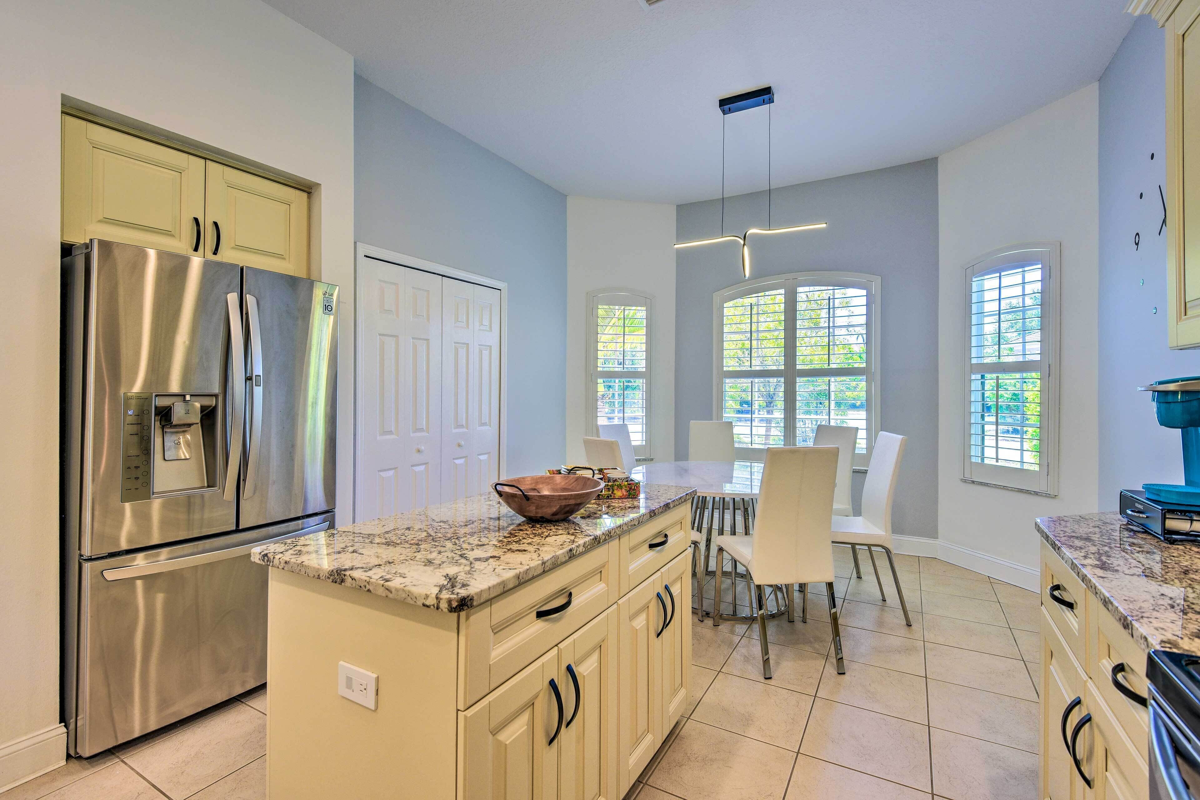 A modern kitchen with a stainless steel refrigerator, a granite countertop, and a dining area with a white table and chairs.