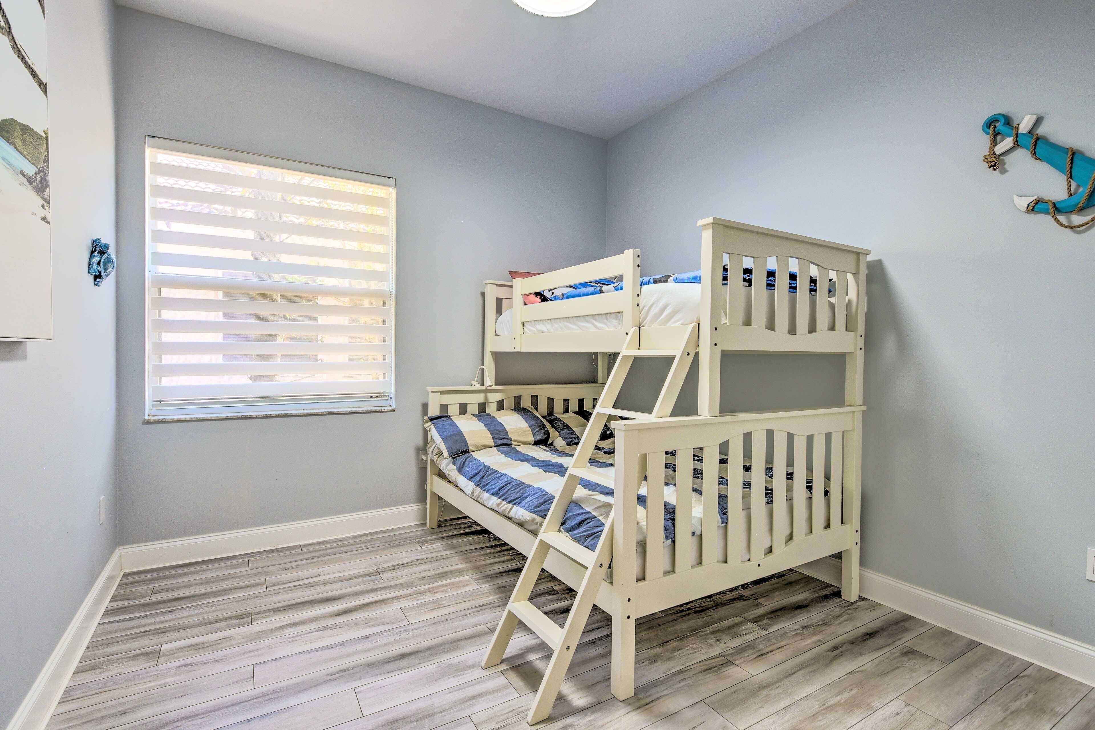 Een kinderbed met twee bedden in een kamer met lichtgrijze wanden en houten vloer.