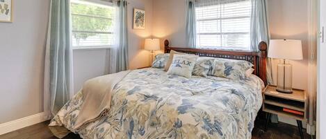 Un dormitorio con una cama, dos lámparas de noche, una mesita de noche y una ventana con cortinas.