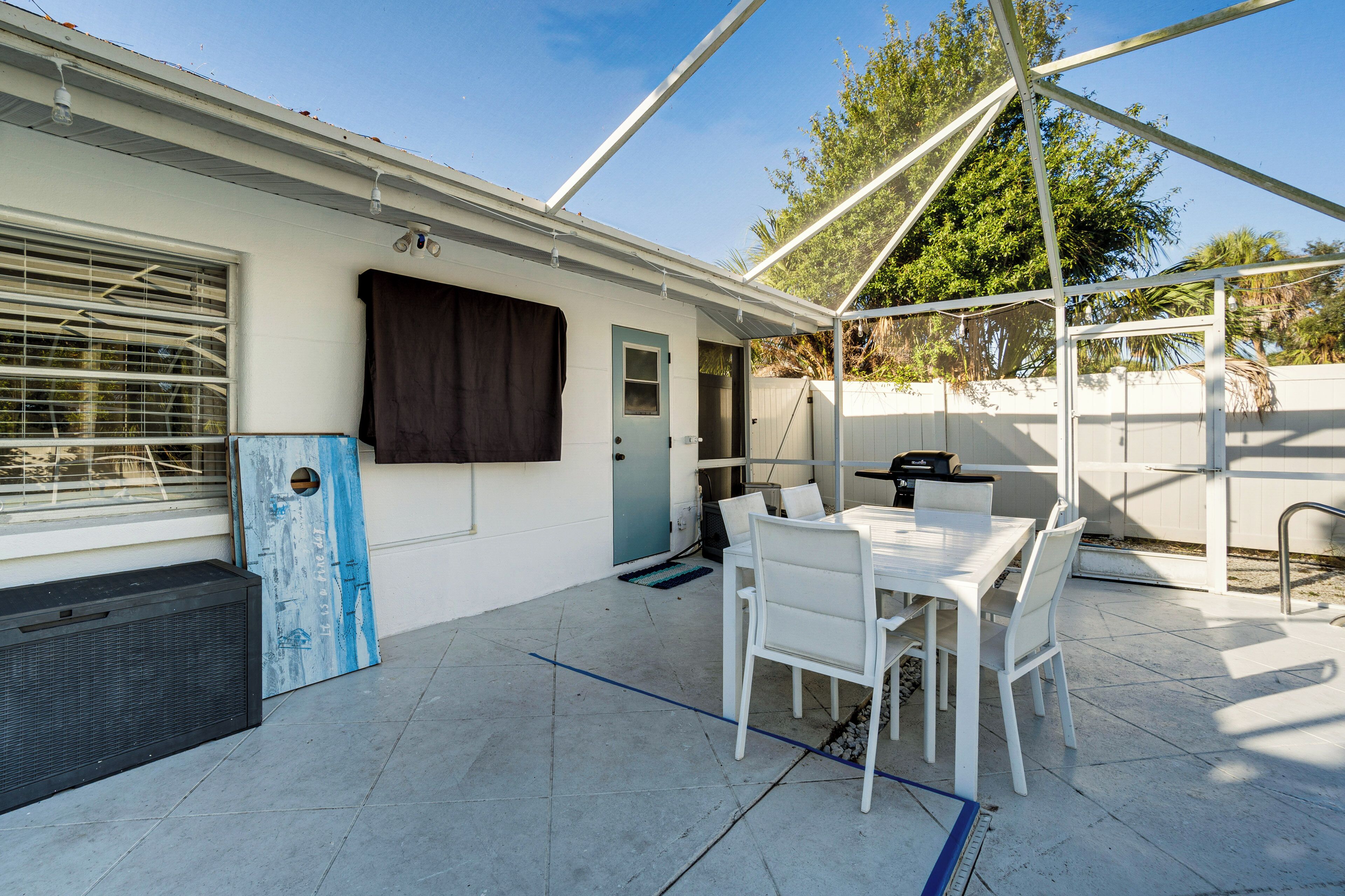 A covered patio area with a white table and chairs, a door, and a window with blinds.