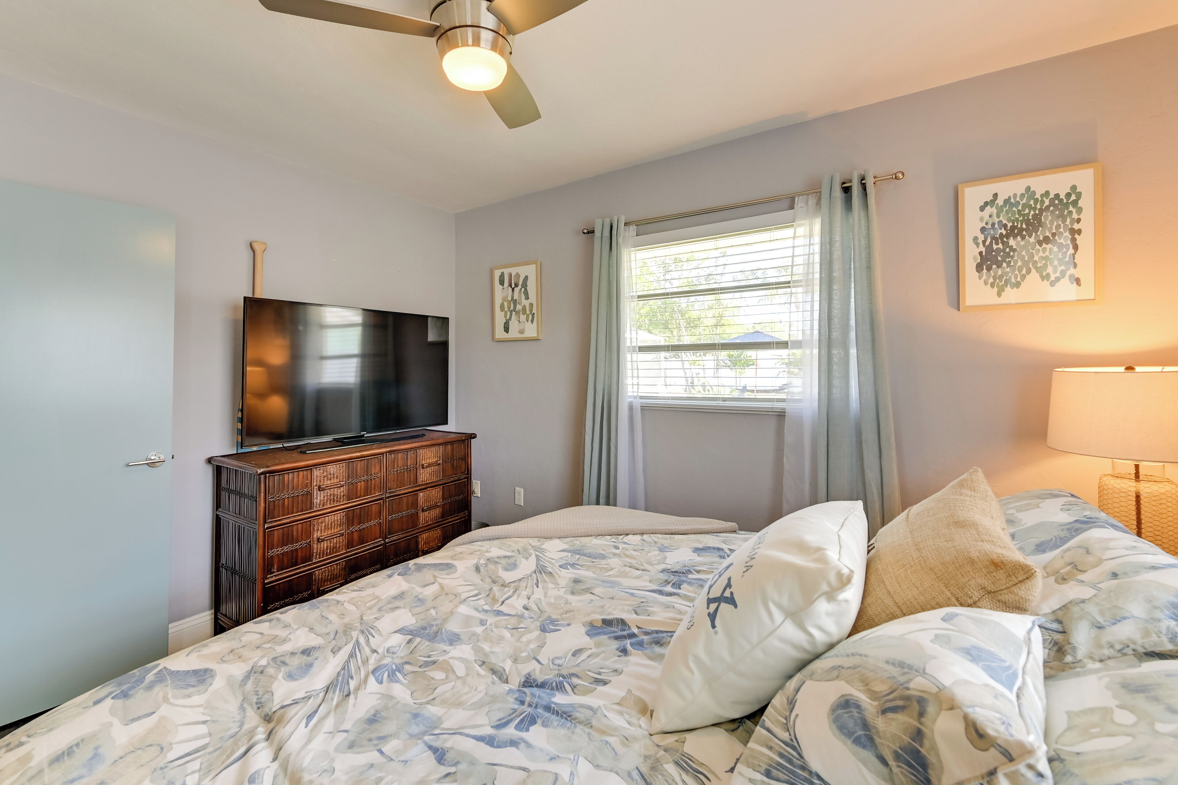 A bedroom with a bed, a dresser, a TV, and a window with curtains.