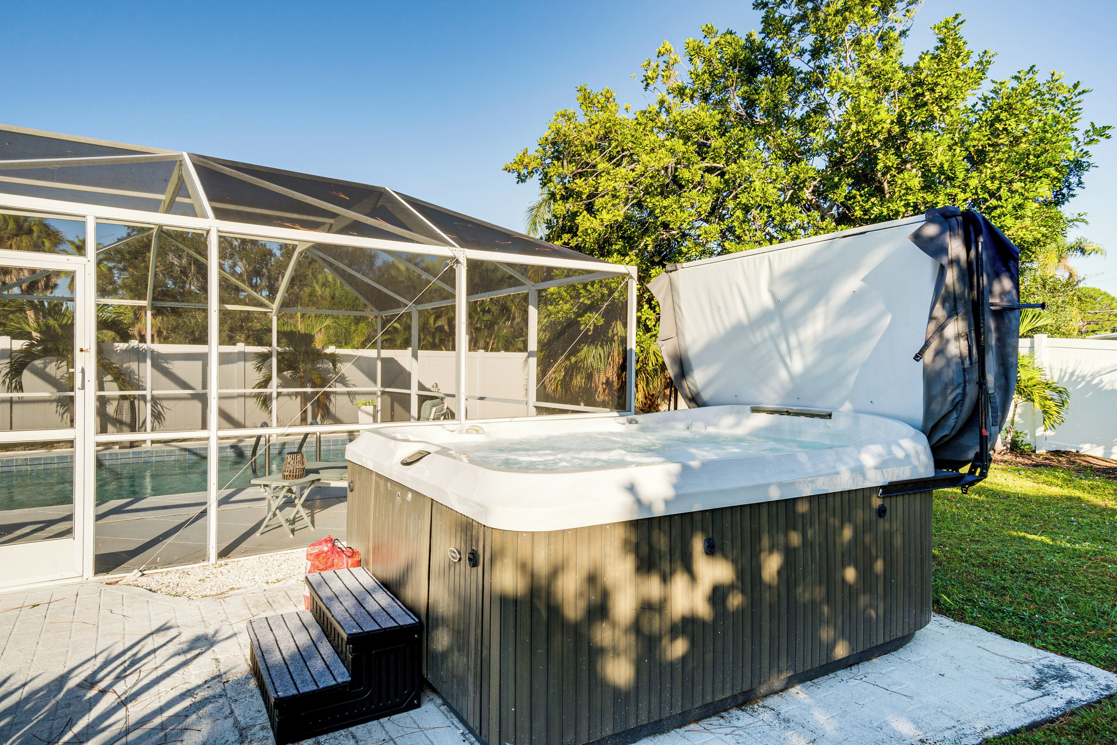 A hot tub with a canopy, a pool, and a patio area with a chair and a small table.