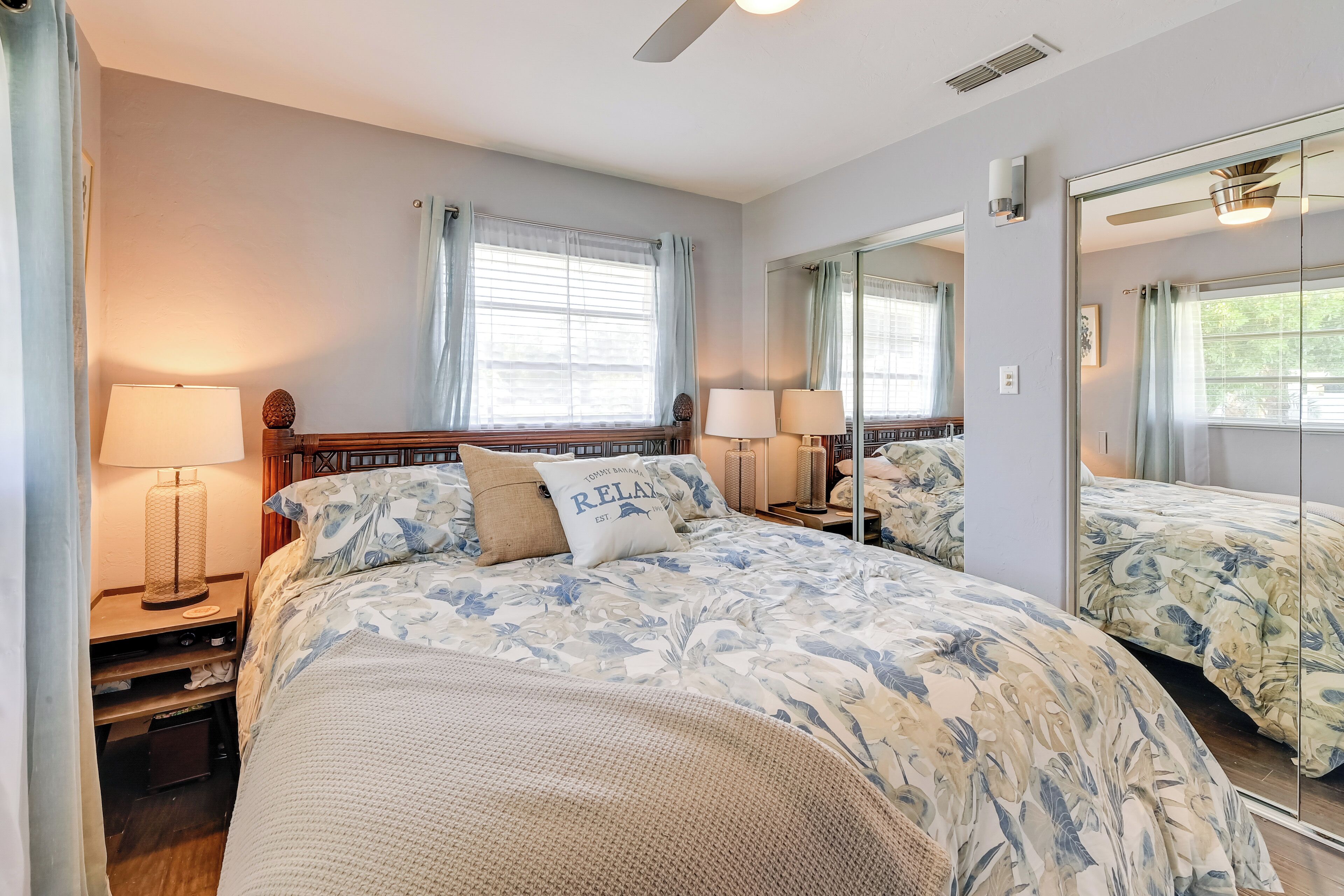 A bedroom with a large bed, two bedside tables, a mirror, and a window with curtains.