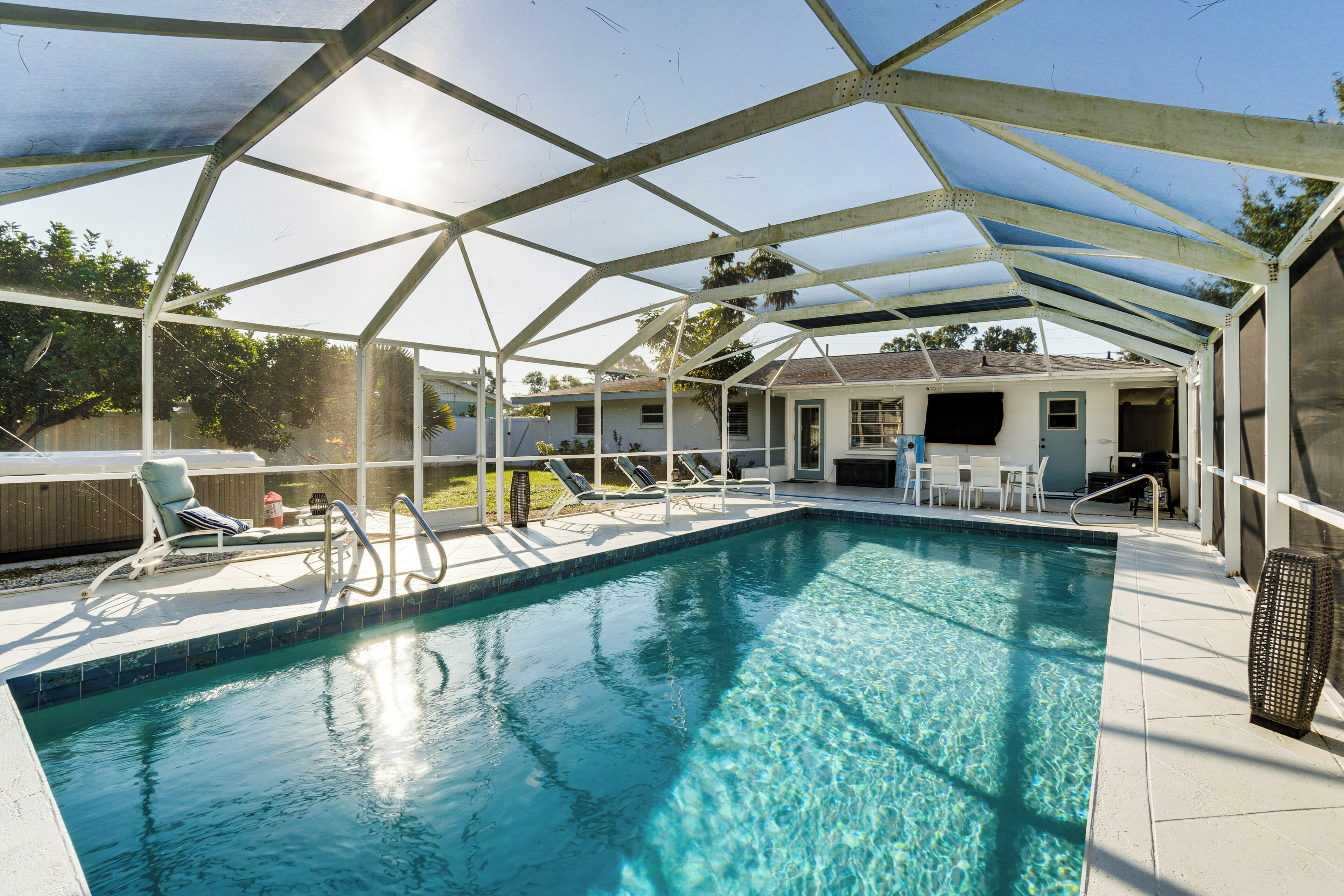 Ein überdachter Pool mit Metallgestell und Sonnensegel, umgeben von Liegestühlen und einer Terrassenfläche.