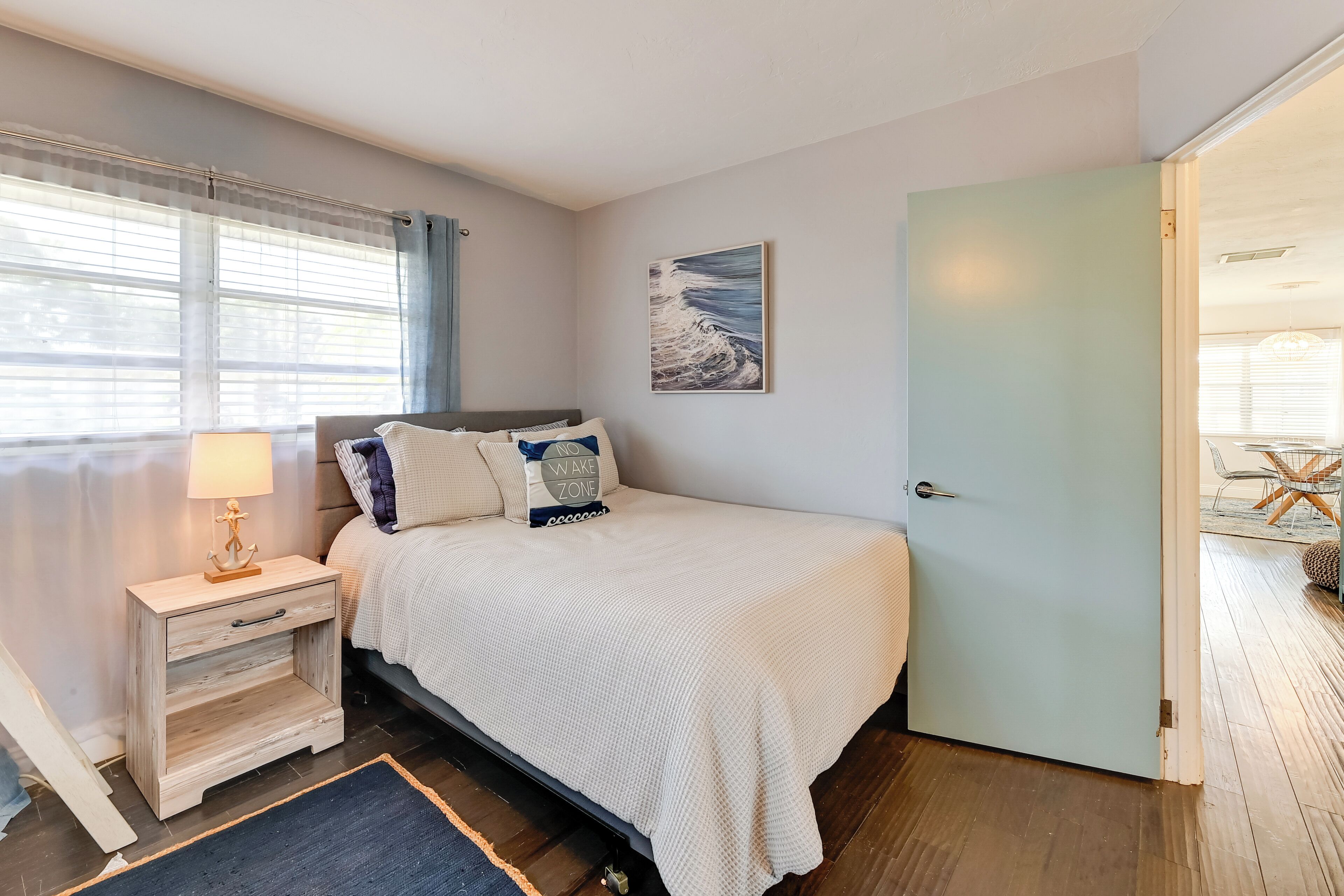Un dormitorio con cama, una mesita de noche, una lámpara, una puerta y una ventana con cortinas.