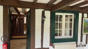 Et værelse med synlige træbjælker, en hvid radiator, et vindue med grøn karm og en hvid stol.