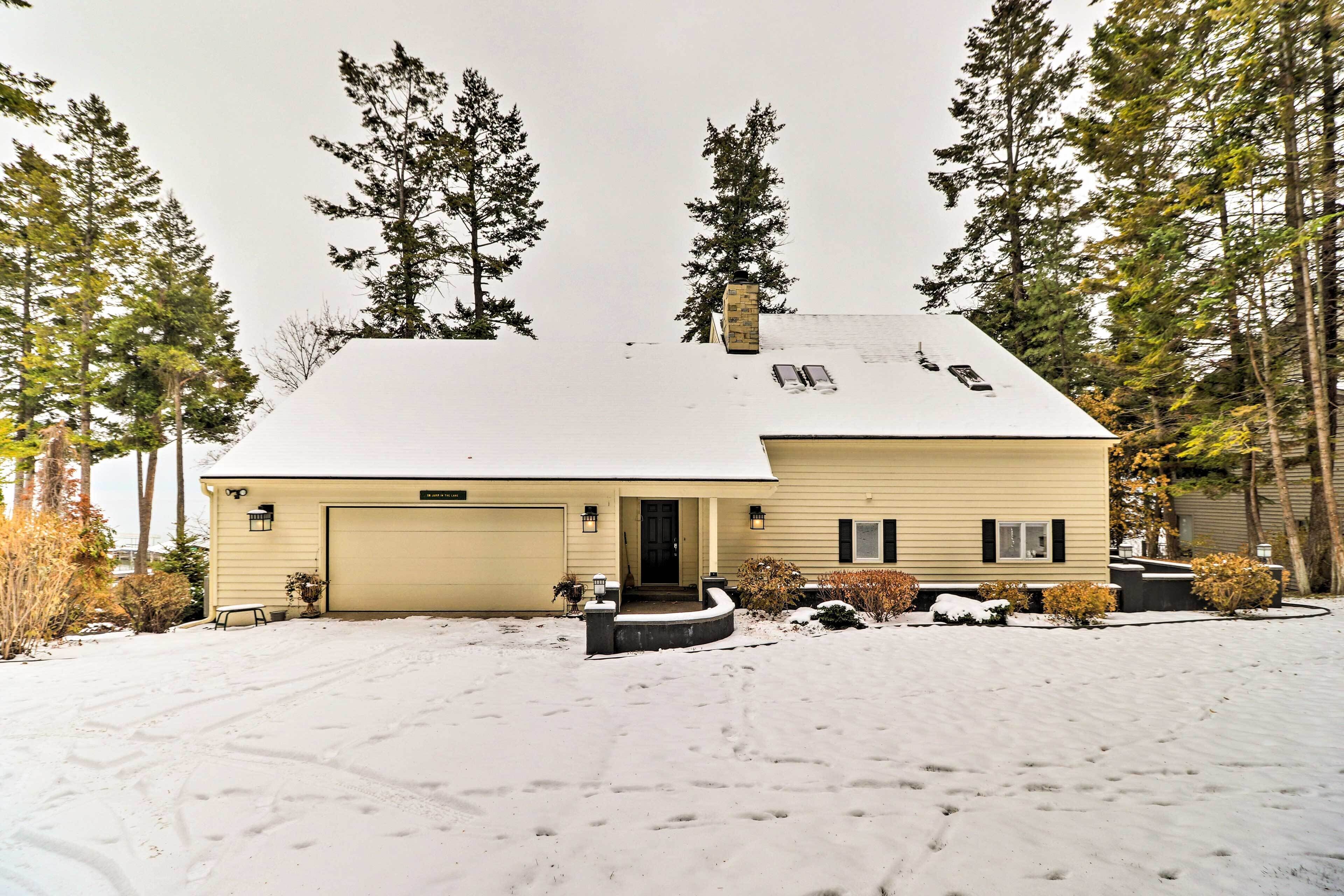 A two-story house with a garage, surrounded by snow-covered ground and tall trees.