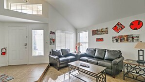A spacious living room with two leather sofas, a coffee table, and a fireplace. There are multiple windows with blinds, a door, and wall art. - Spacious Las Vegas Home - Near Golfing & Hiking! (Las Vegas)