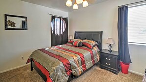 A bedroom with a bed, a nightstand, a lamp, a ceiling fan, a window with curtains, and a wall-mounted mirror. - Spacious Las Vegas Home - Near Golfing & Hiking! (Las Vegas)