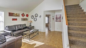 A living room with a leather sofa, coffee table, and wall art. A staircase leads to another room. - Spacious Las Vegas Home - Near Golfing & Hiking! (Las Vegas)