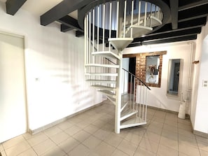 A modern interior with a spiral staircase, a brick wall, and a tiled floor. - Arsuzon - Josse - Gîte (JOSSE)