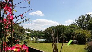 A backyard with a swing set, a small pool, and a garden area with flowering plants. - Arsuzon - Josse - Gîte (JOSSE)