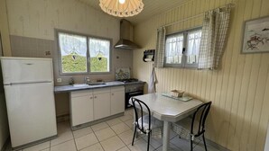 A compact kitchen with a white refrigerator, a stove, and a dining table with two chairs.