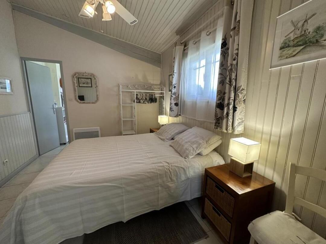 Un dormitorio con cama, mesitas de noche, un armario y una ventana con cortinas.
