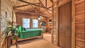 Dormitorio de cabaña de madera con cama, escritorio, silla y ventana con cortinas.