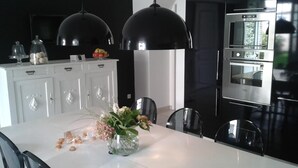 A modern kitchen with a white dining table, black pendant lights, and stainless steel appliances. - Lajenet - Benquet - Gîte (BENQUET)