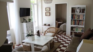 A living room with a checkered floor, a white coffee table, wicker chairs, a bookshelf, and a television. - Lajenet - Benquet - Gîte (BENQUET)