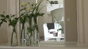 A room with a large mirror reflecting a white sofa, a small table with a lamp, and three clear vases with plants. - Lajenet - Benquet - Gîte (BENQUET)