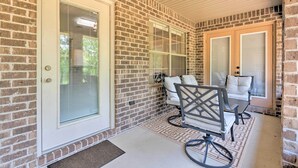 A covered porch with brick walls, a sliding glass door, and two chairs with cushions.