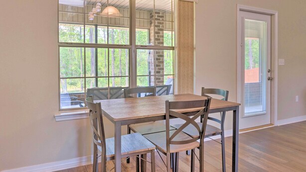 A dining area with a table and chairs, large windows with a view of trees, and a door with blinds.