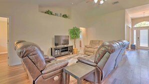 A spacious living room with leather sofas, a TV, and a ceiling fan.
