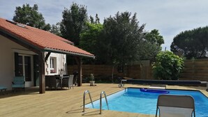 A wooden deck with a swimming pool, a covered patio area, and a fenced yard. - Gîte de Linxe - Linxe (LINXE)